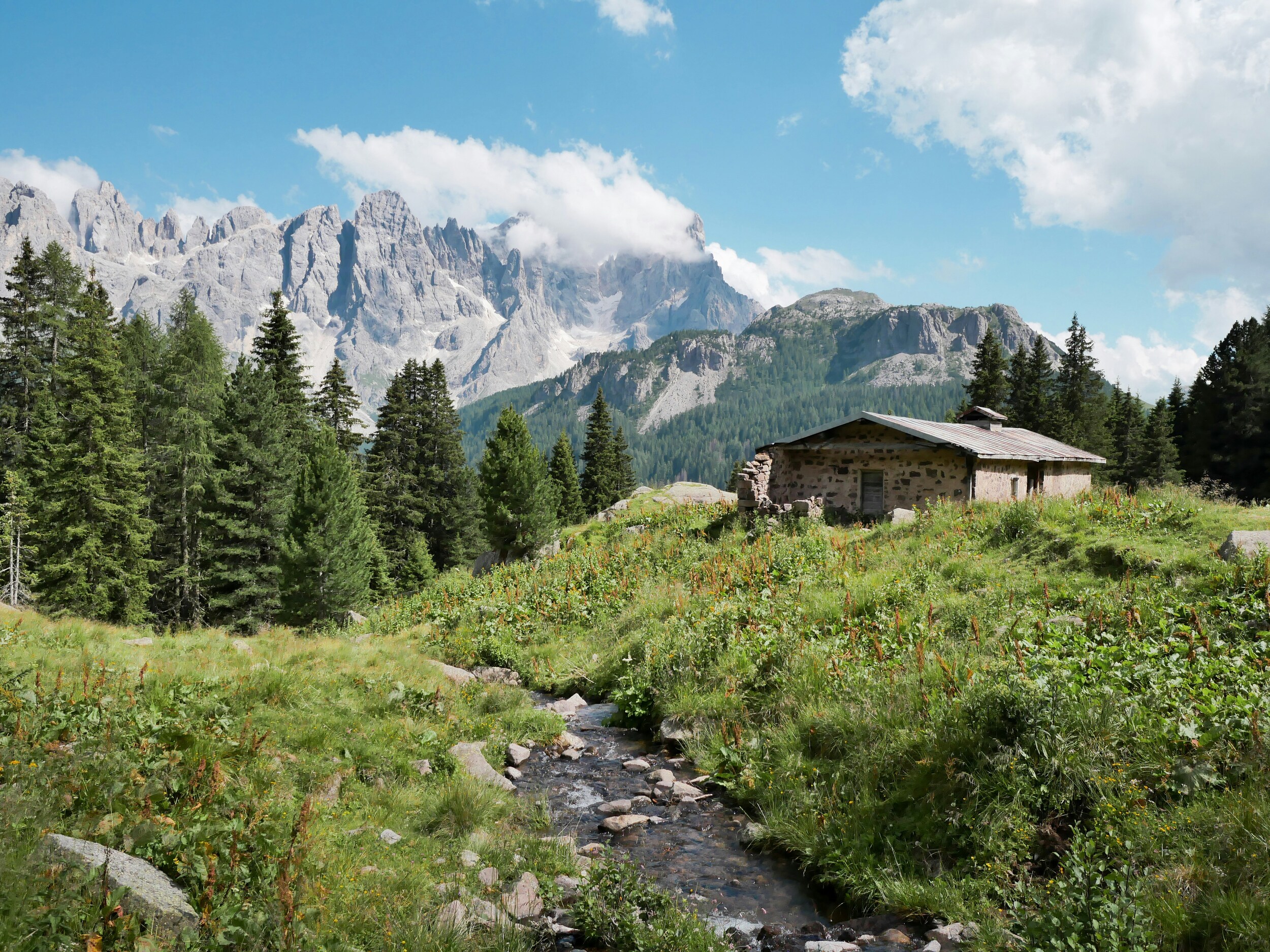 Small river, stone mountain hut and mountains in the background