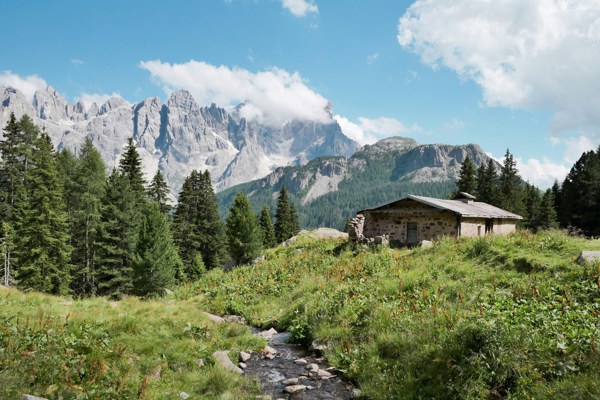 Small river, stone mountain hut and mountains in the background