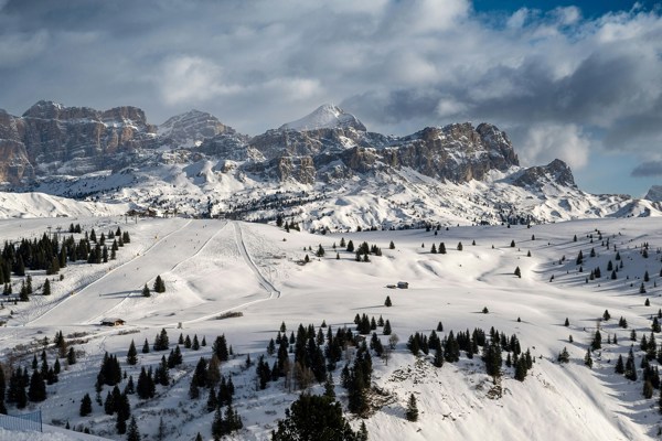 Ski slopes with skiers, lifts, snow-covered mountains and cloudy sky