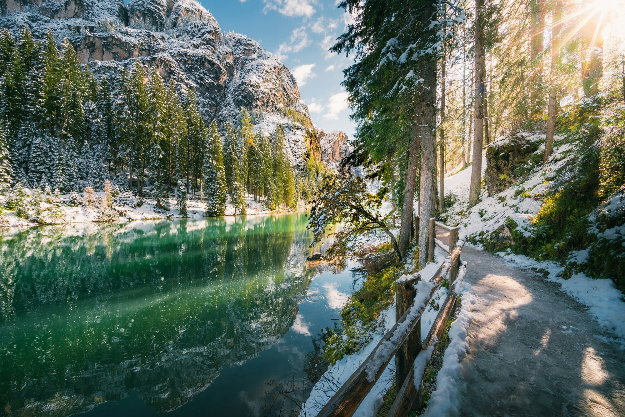 Lightly snow-covered footpath on the shore of a turquoise mountain lake