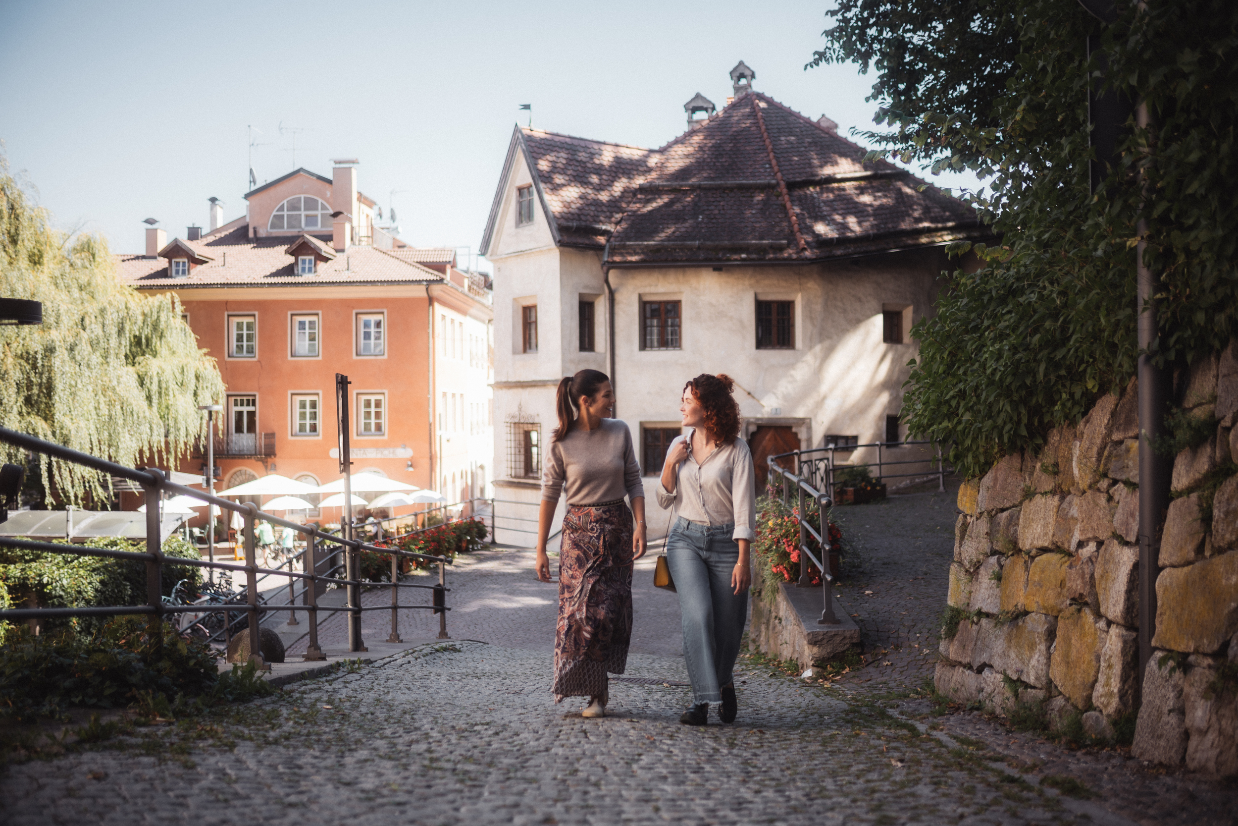 Two women walk up a cobbled street in a city