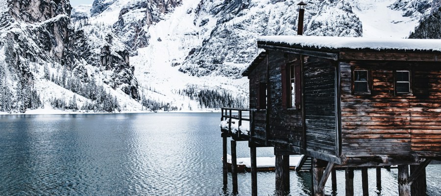 Wooden hut on stilts in the water of a lake, snow-covered mountain in the background