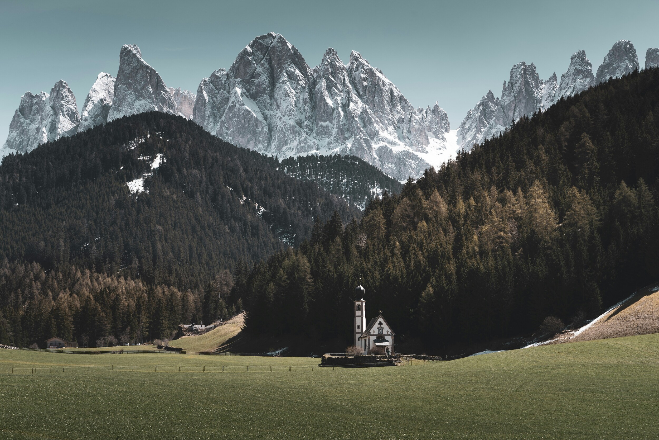 Small church on a meadow in front of woods and mountains