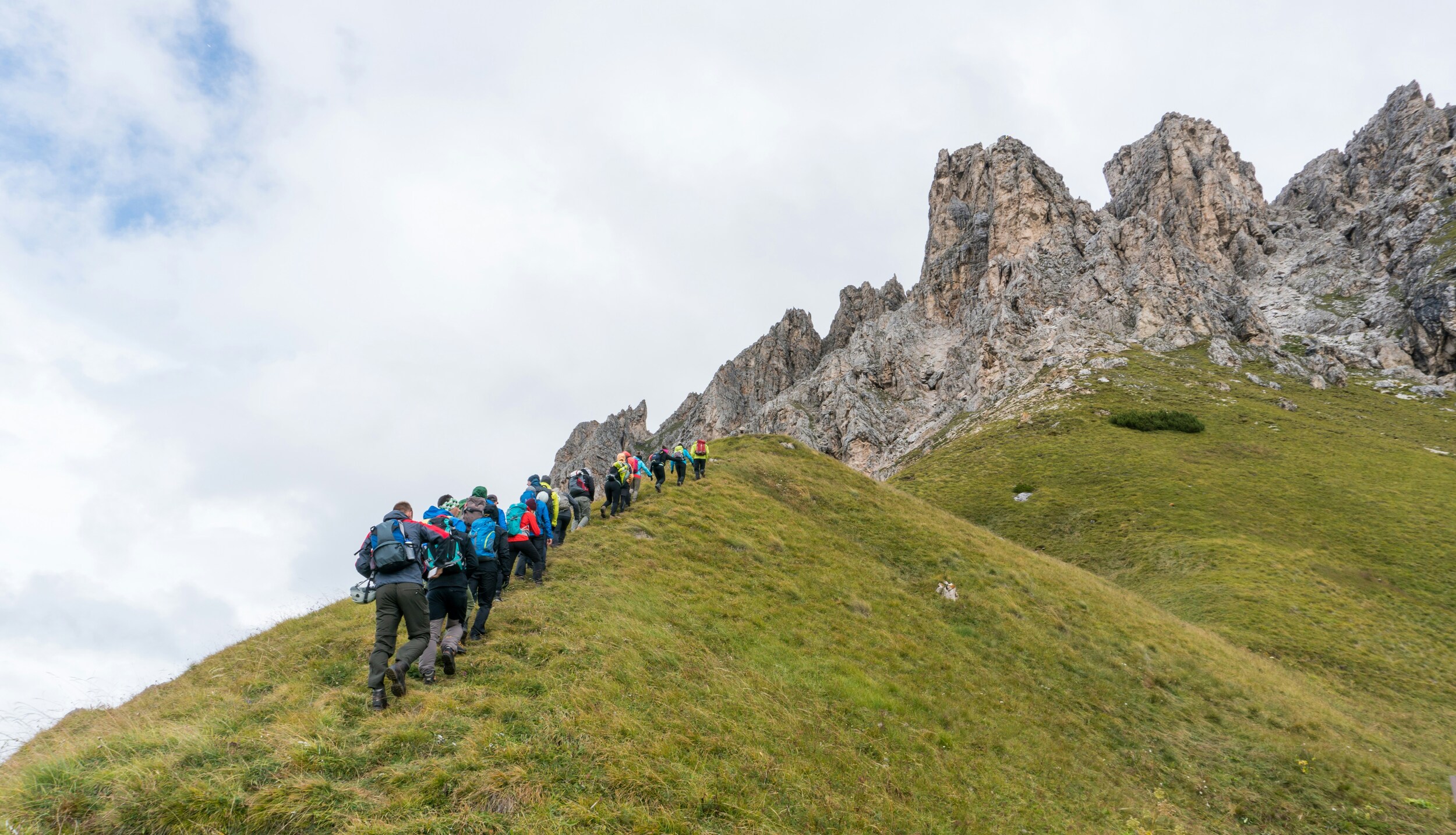 Group of hikers ascending a green mountain ridge reaching the rocks