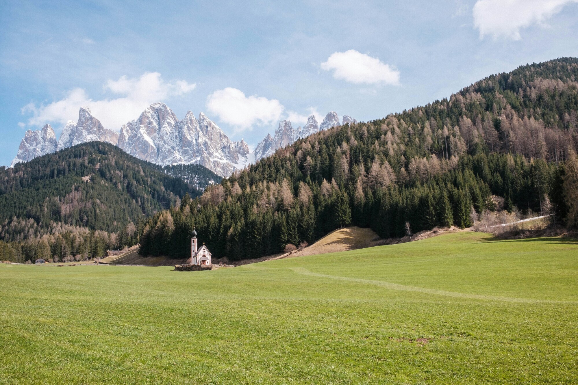 Small church on a meadow in front of woods and mountains