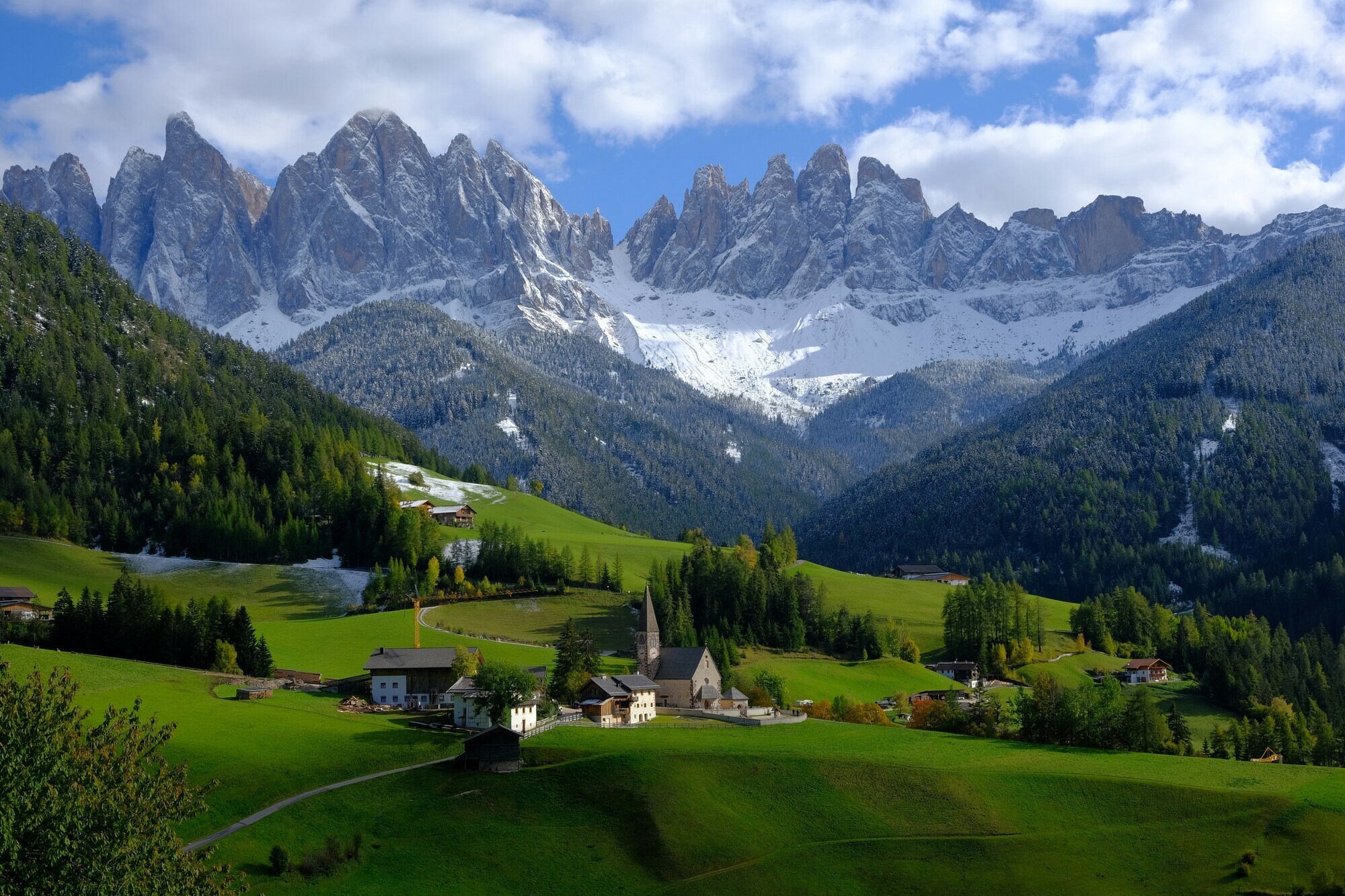 Mountain village with church, snow-covered peaks & green meadows