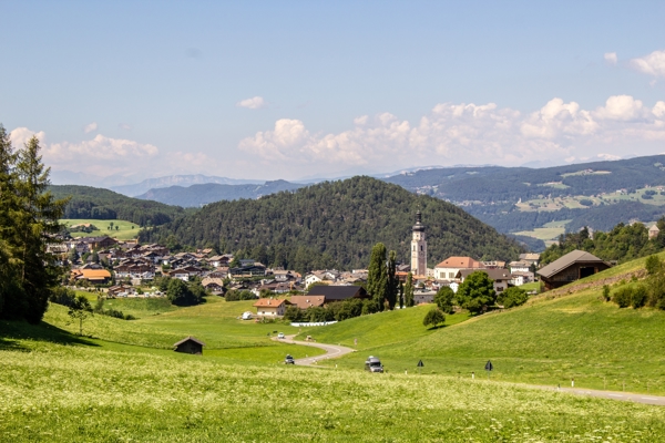 Hilly landscape with green meadows, forests and houses of a village in the centre