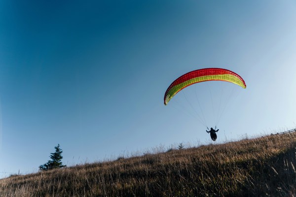 Paraglider with red and yellow paraglider taking off from a mountain meadow