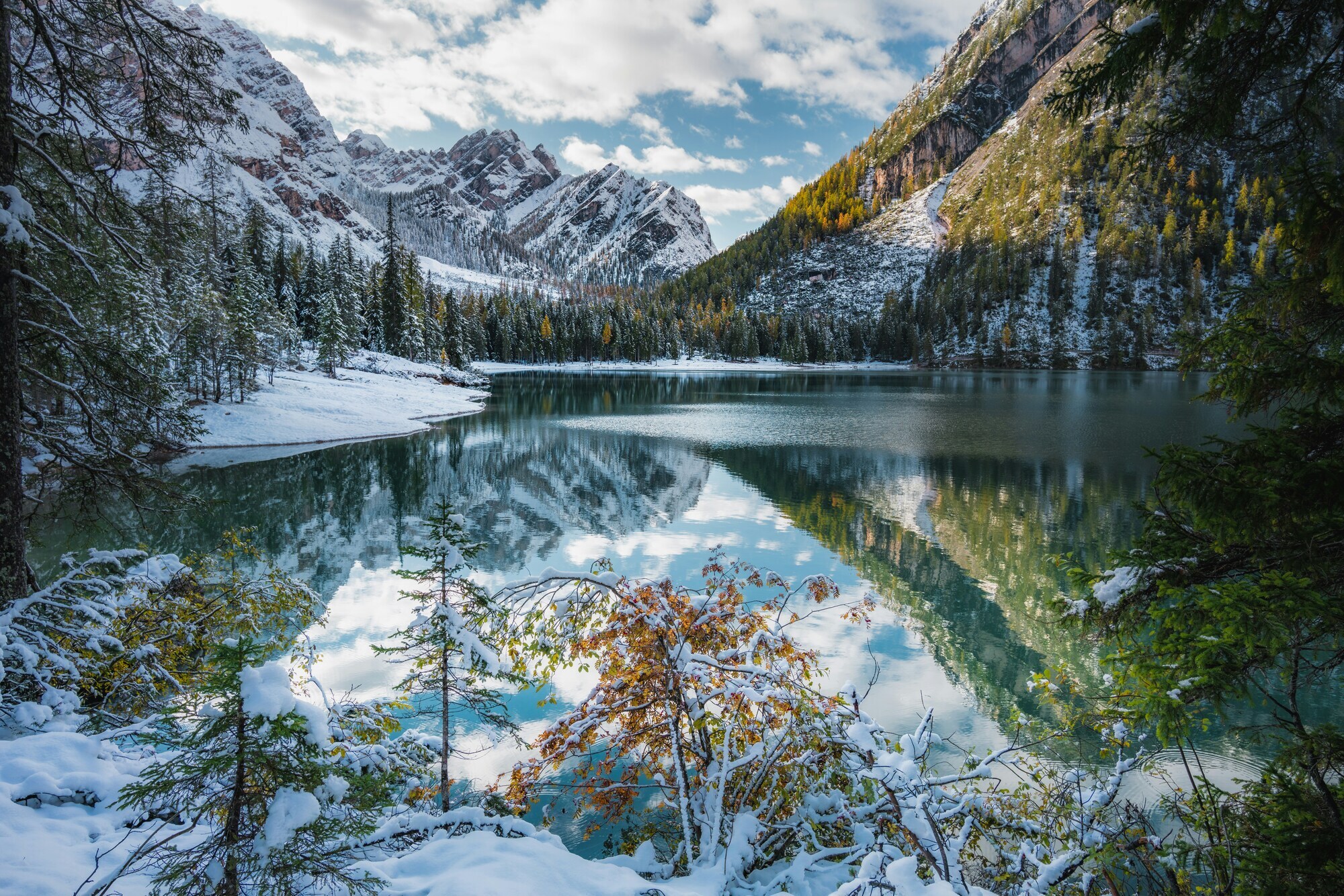 Snow-covered mountain landscape with lake, forest and rock faces