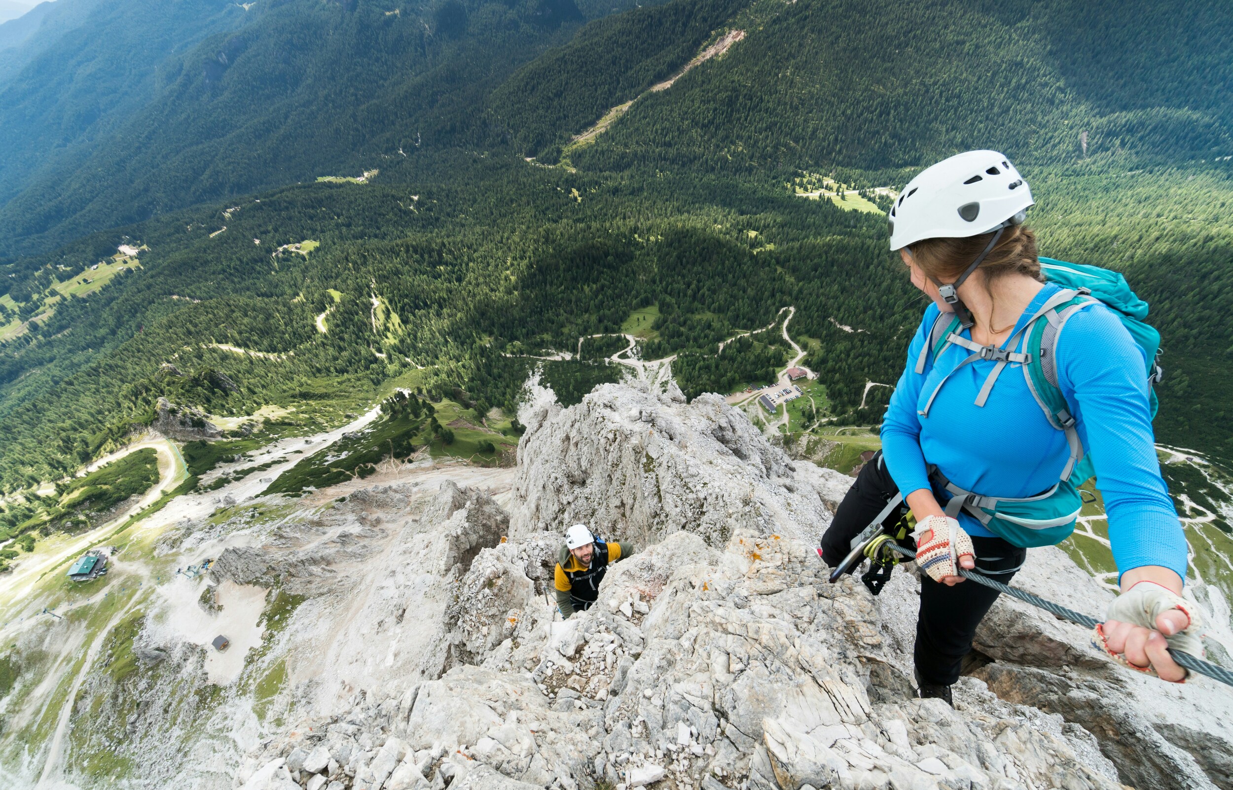 Two climbers on a rocky via ferrata high above a wooded valley