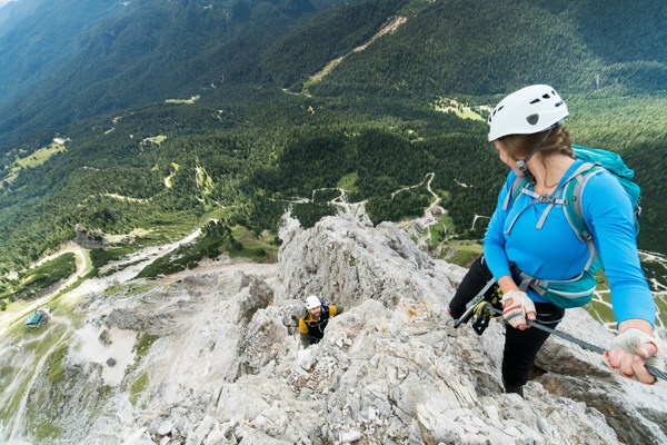 Two climbers on a rocky via ferrata high above a wooded valley