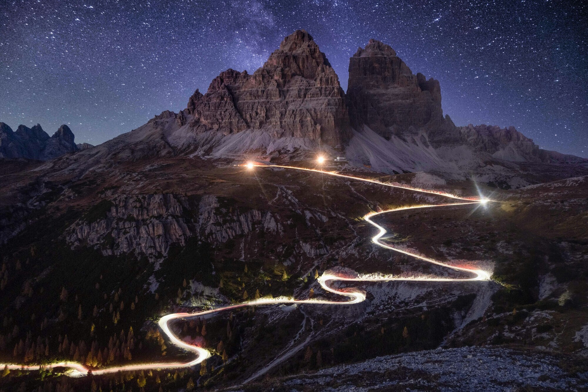 Lit, winding pass road to a hut and peaks under the stars