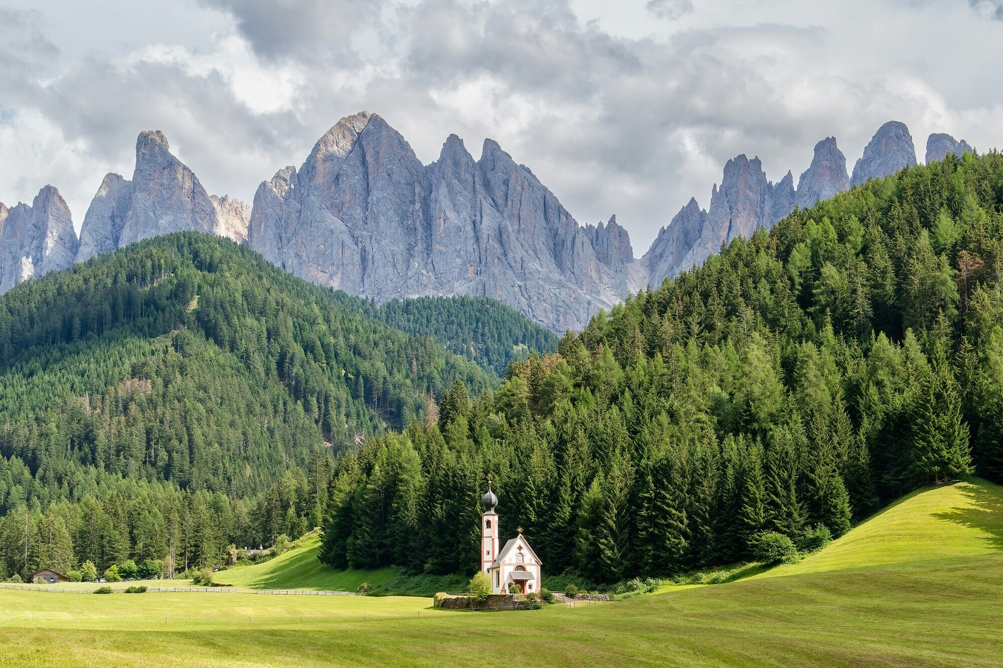 Small church on a meadow in front of woods and mountains