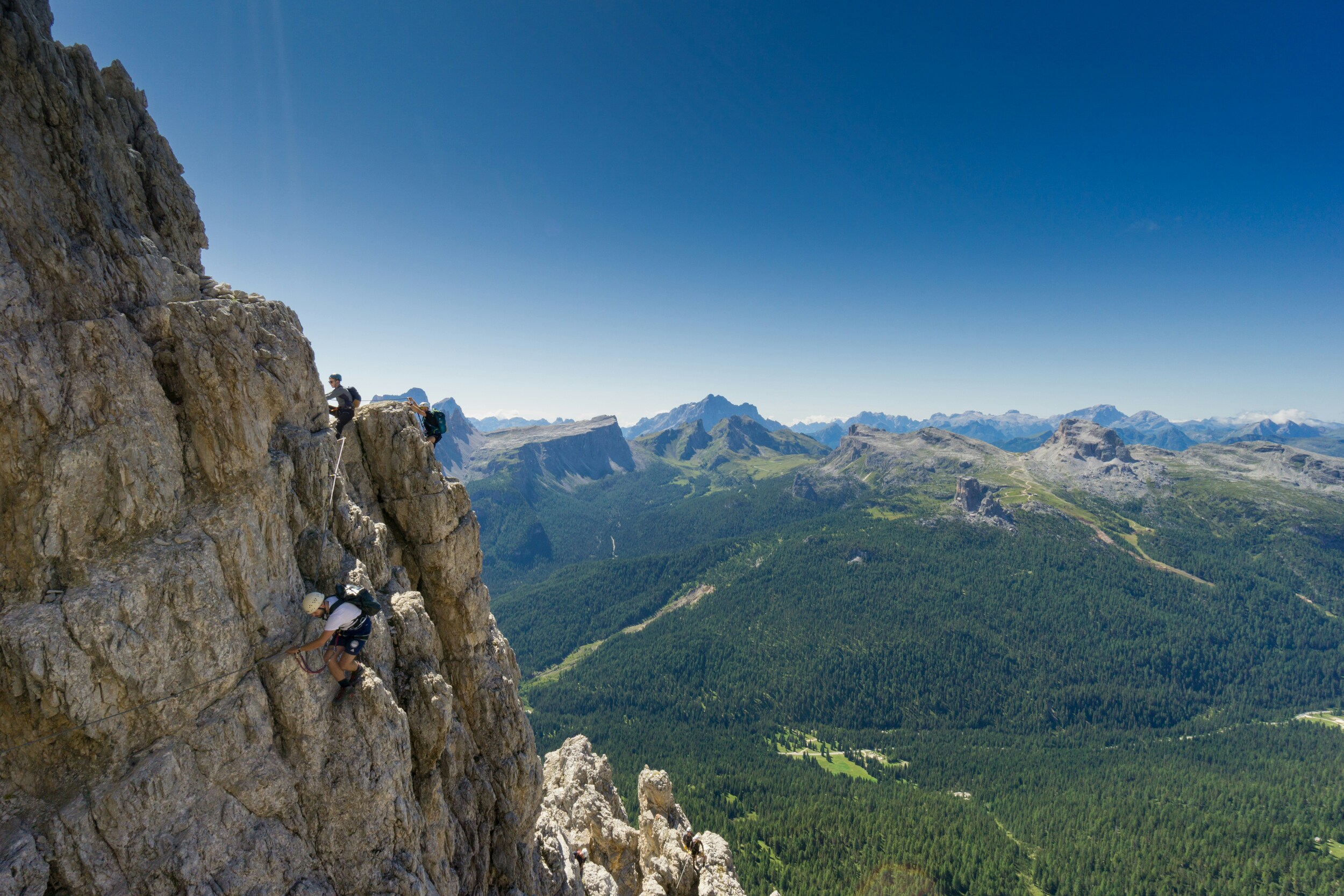 Climbers on a rock wall with mountains and forest in the background