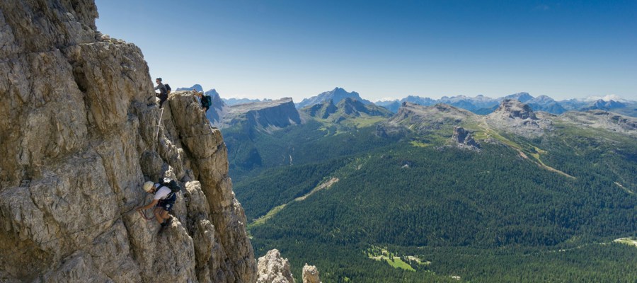 Climbers on a rock wall with mountains and forest in the background