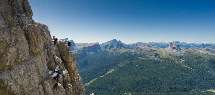 Climbers on a rock wall with mountains and forest in the background