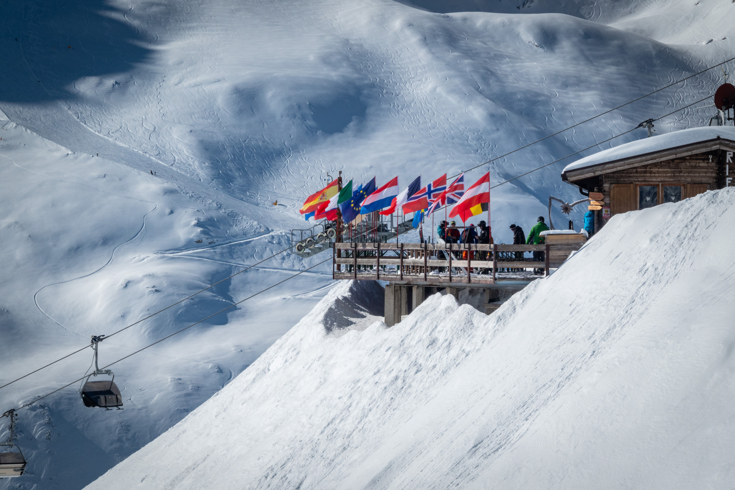 Restaurant terrace with flags and ski lift on snow-covered mountains