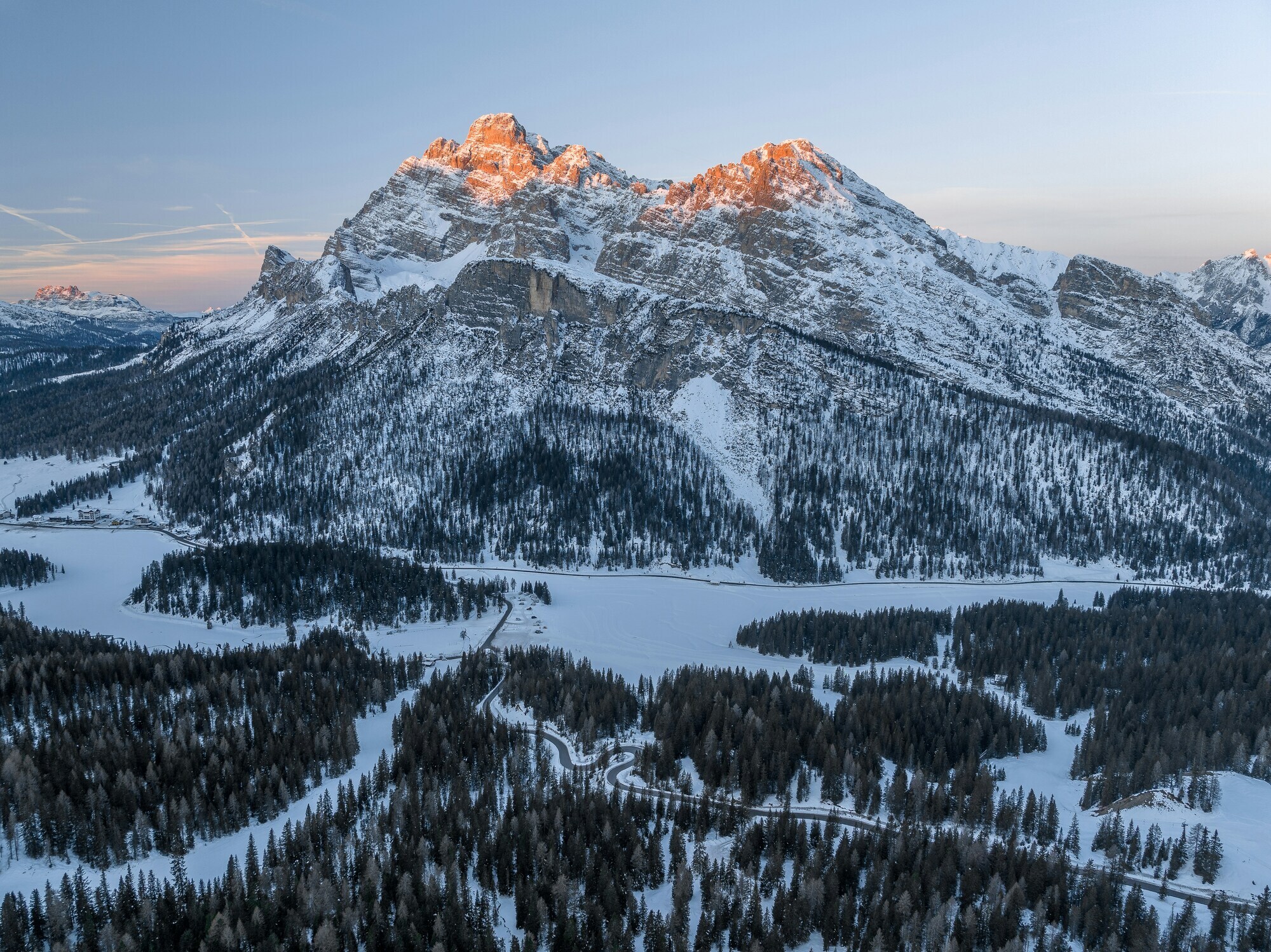 Snow-covered valley with winding road, woods and mountains