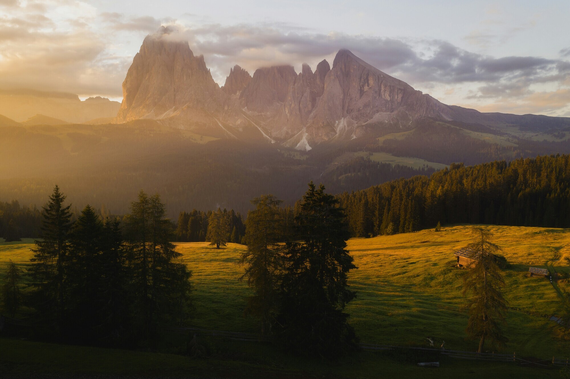 Sun shines through clouds on mountain peaks and meadows