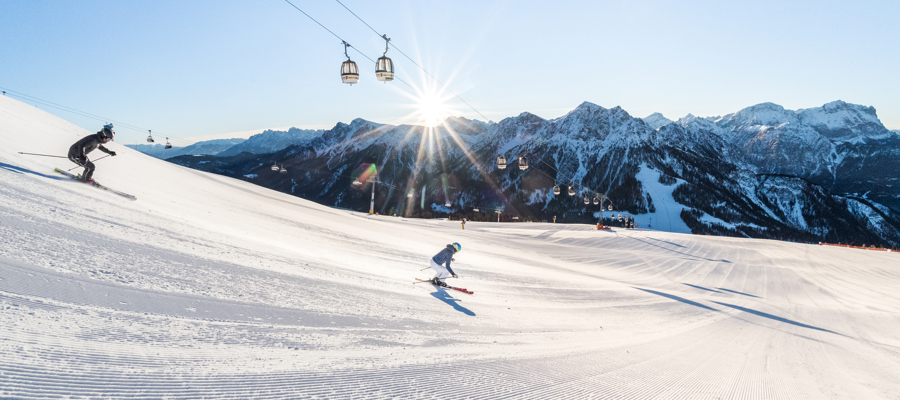 2 skiers on a freshly groomed slope in glorious winter sunshine