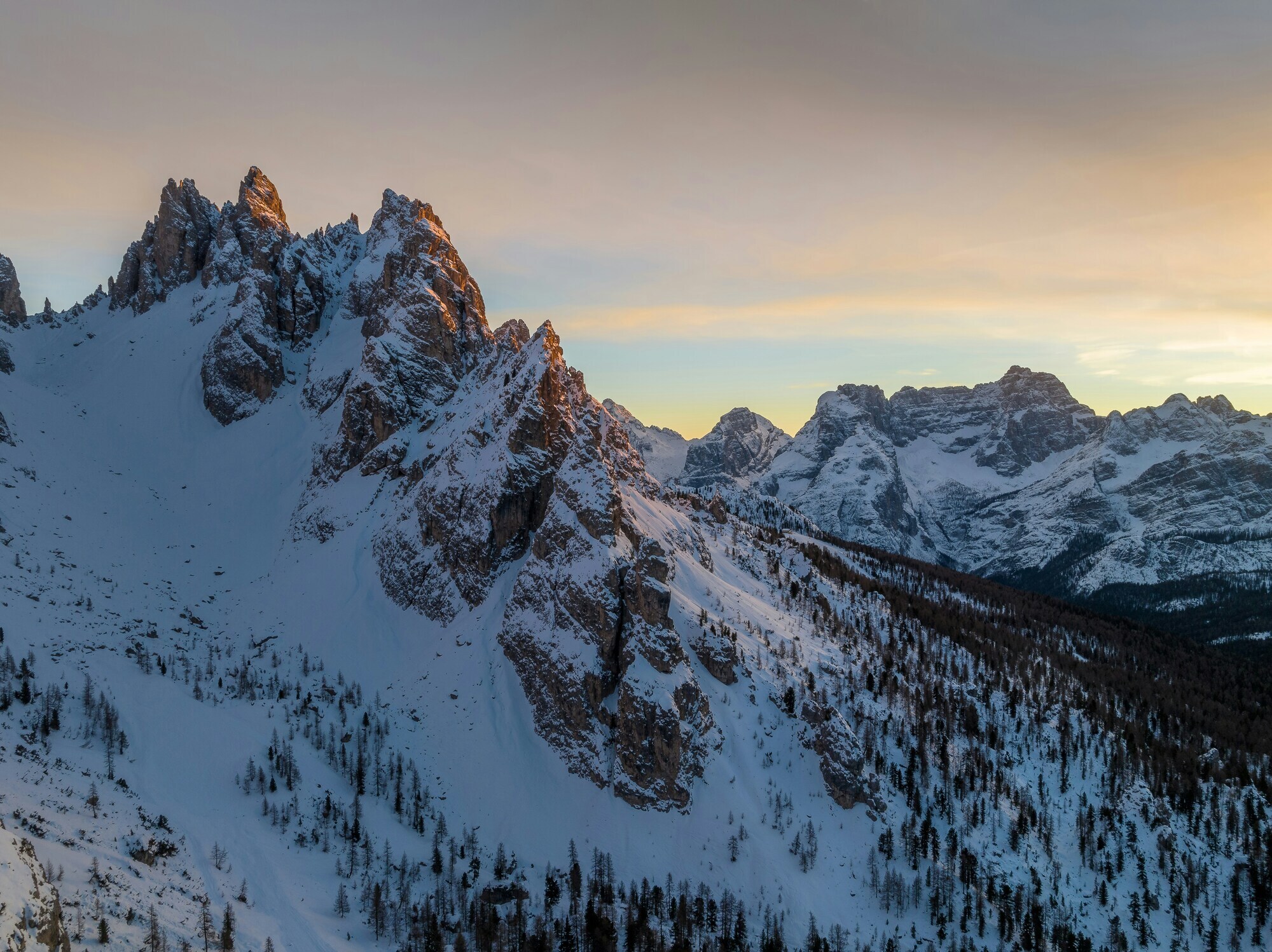 Snow-covered mountain landscape with trees at sunset