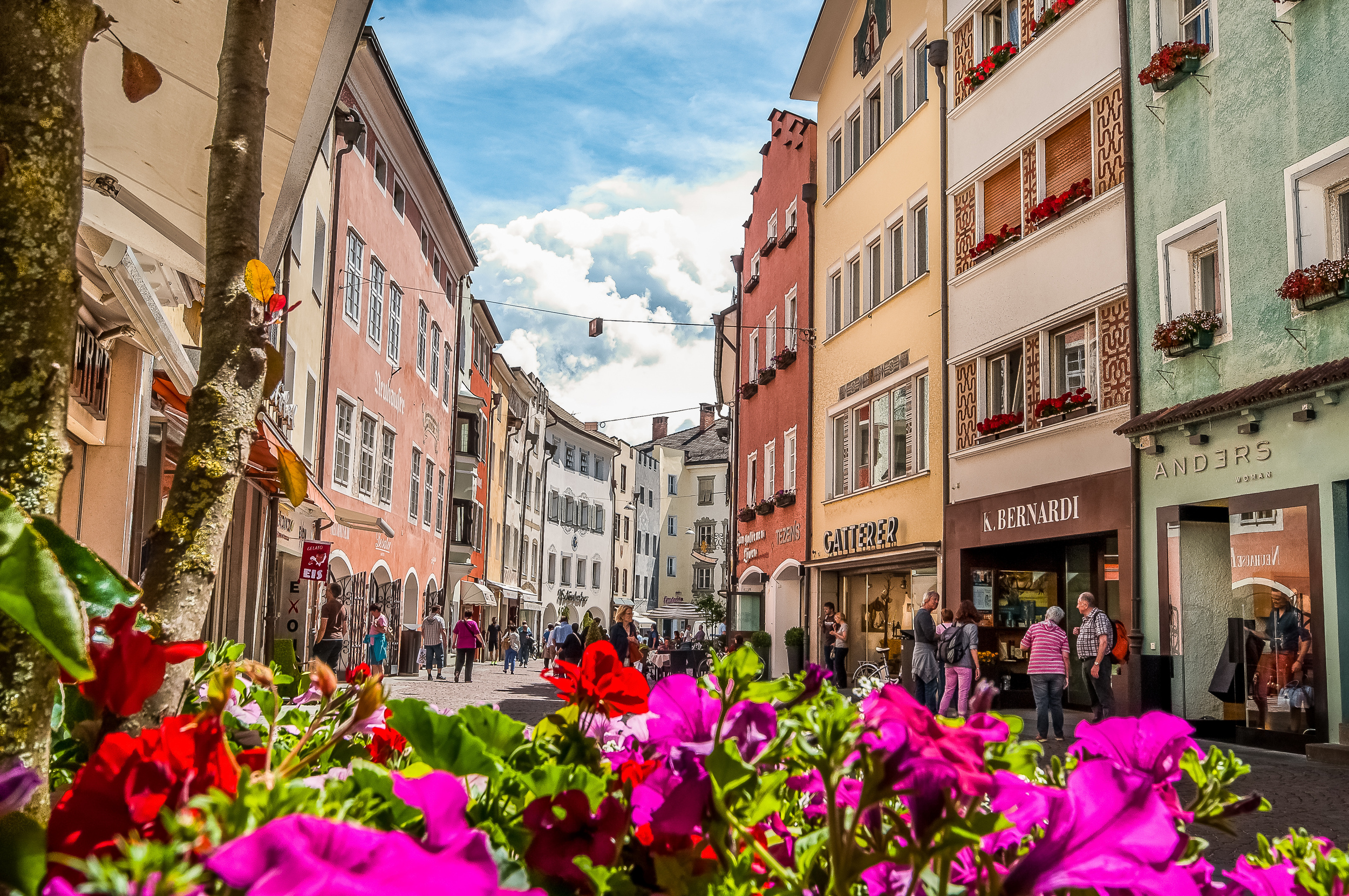 Colourful house facades on both sides of a pedestrian street, pink-red flowers in the foreground