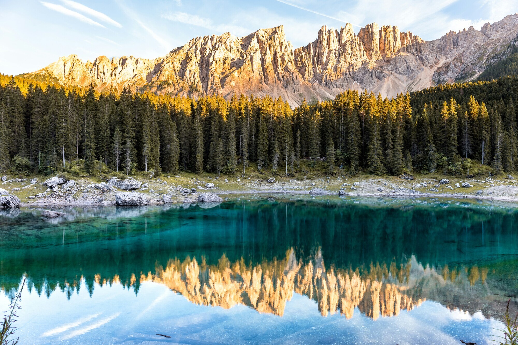 Brightly lit rock formation and trees lying in the shade are reflected in the water of a lake