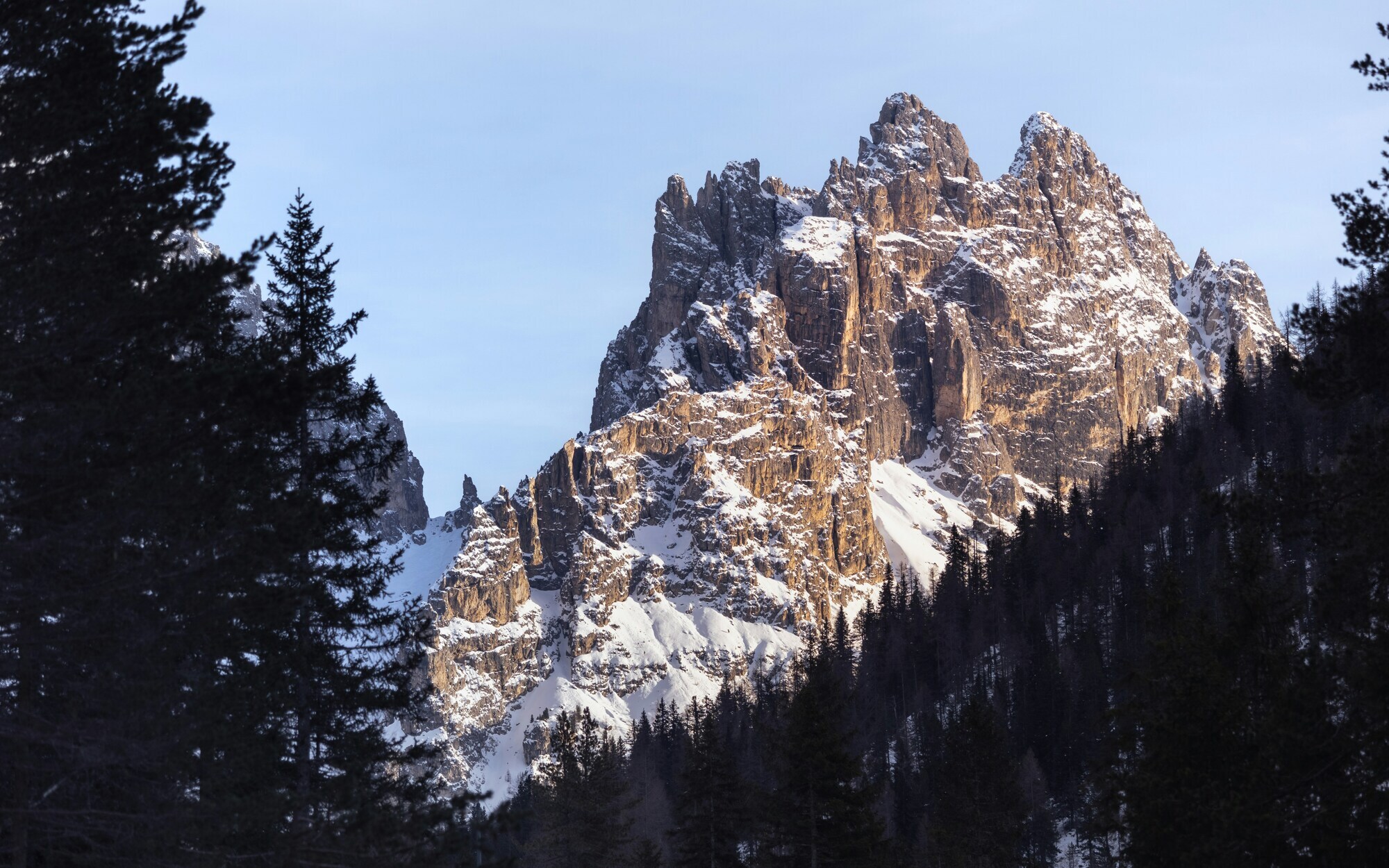 Rugged Dolomites peaks covered in snow, with dark trees