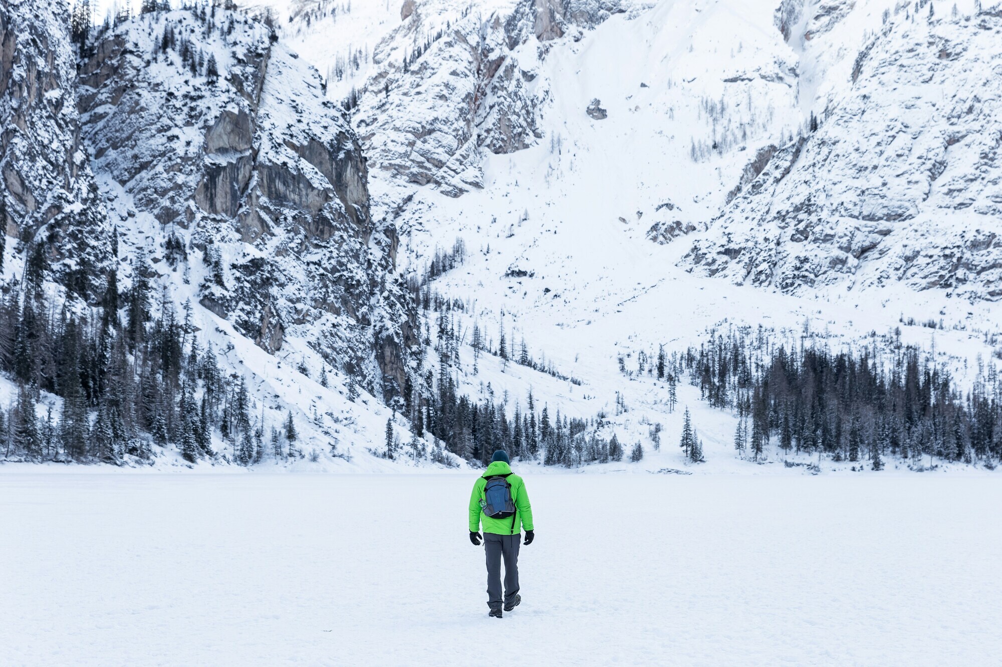 Winter hiker with a bright green jacket in the middle of a snow-covered mountain landscape