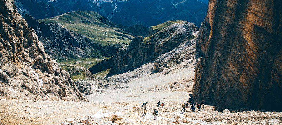 Hikers descending a steep slope near a rock wall