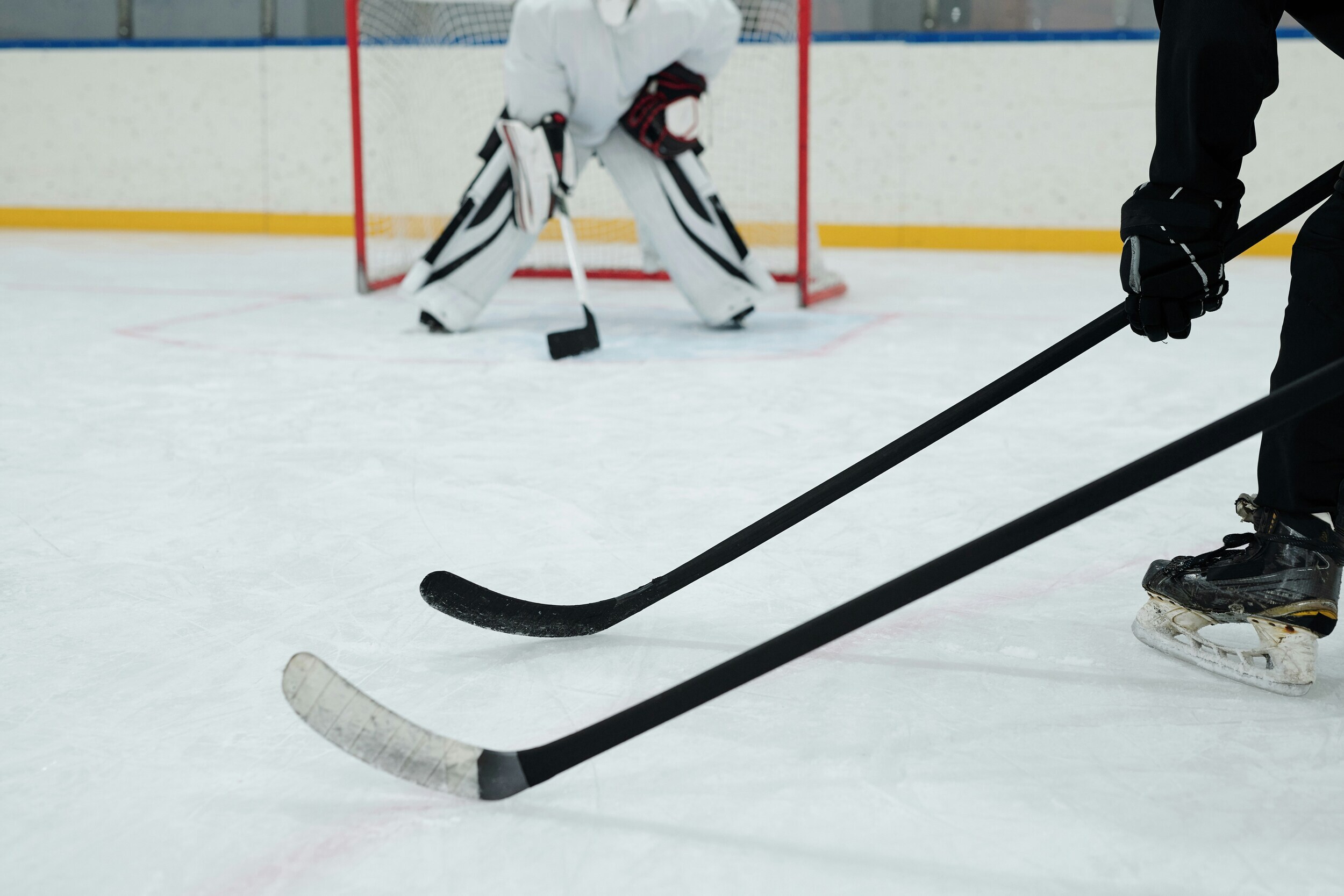 Partial view of hockey goalie and 2 players with hockey sticks waiting in front of the goal