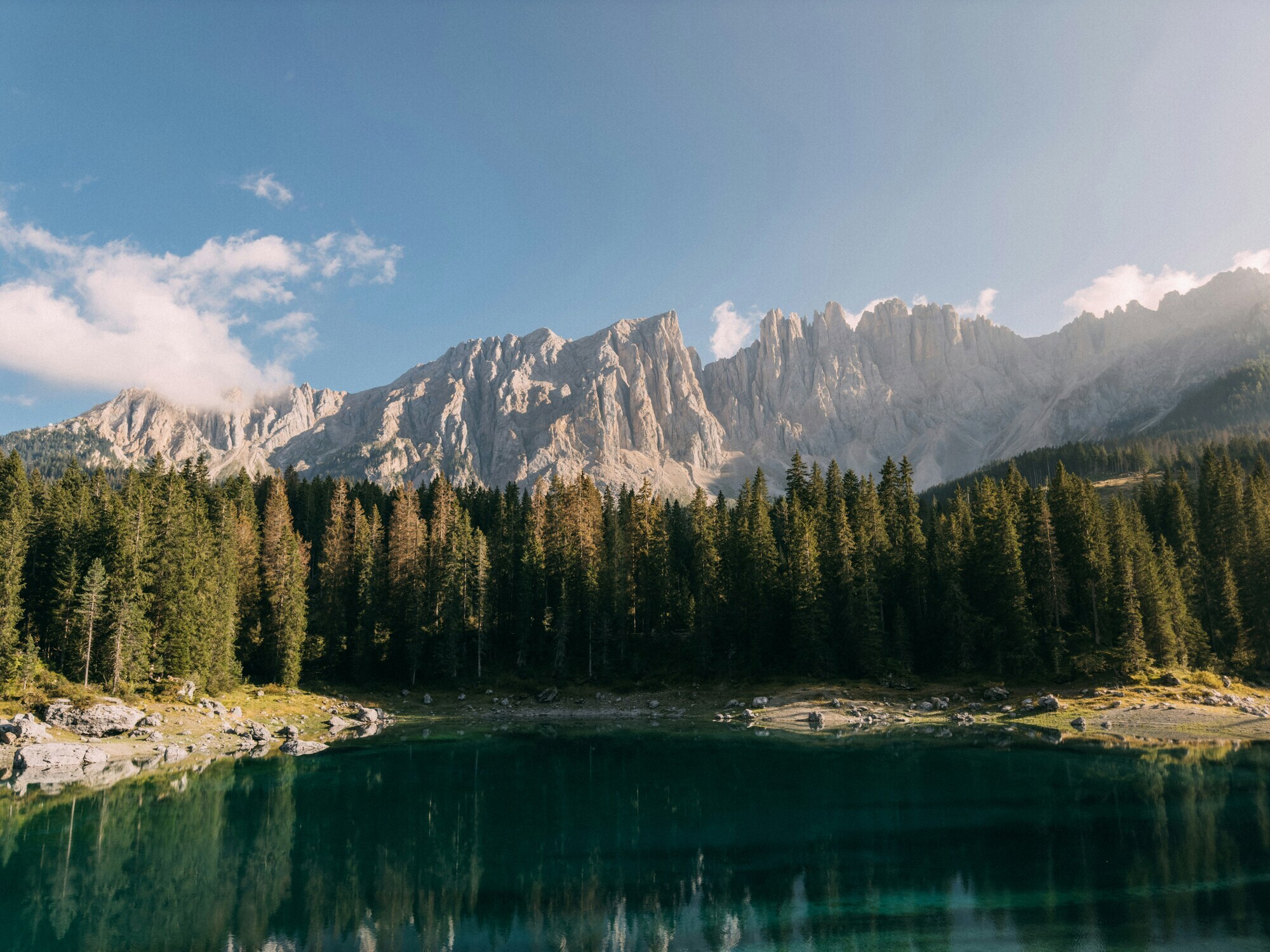 Dark green lake, framed by trees and mountains in bright sunshine