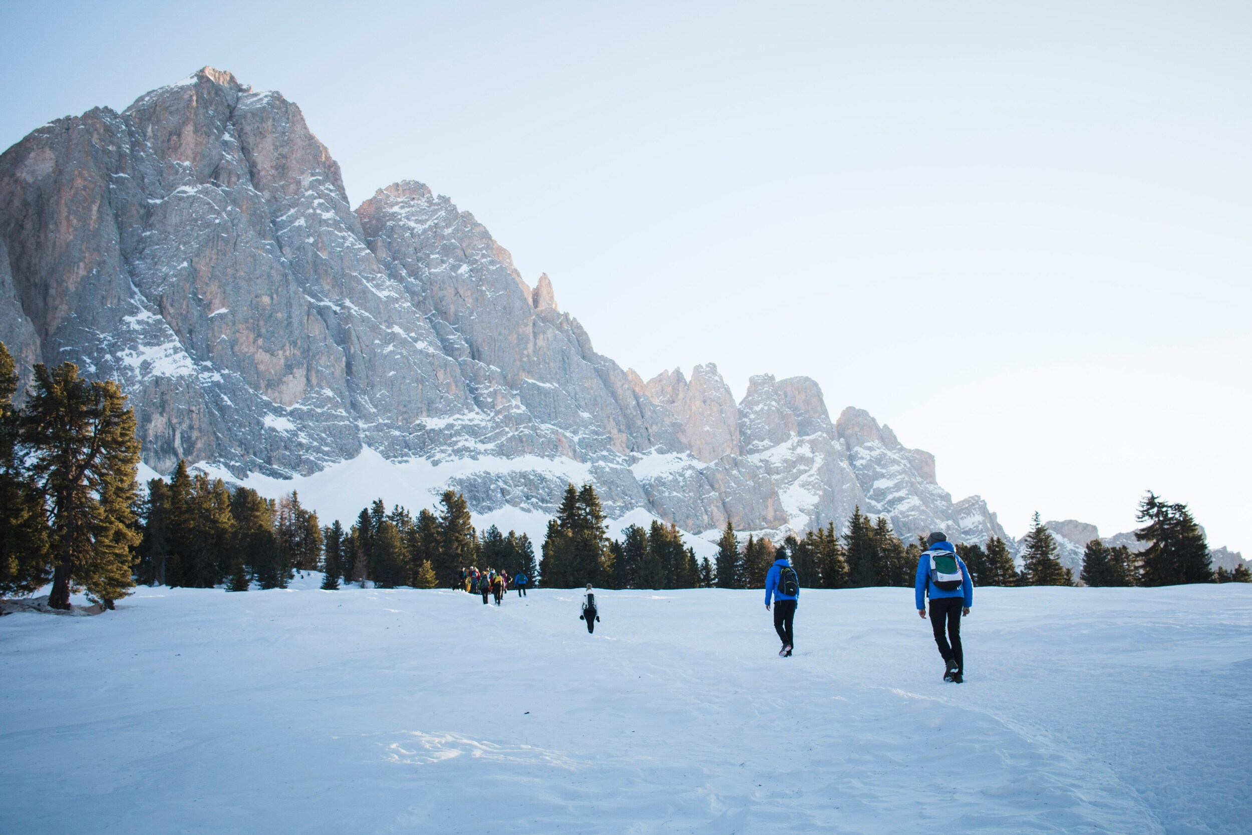 Hikers walking on a flat snow-covered area at the food of mountains