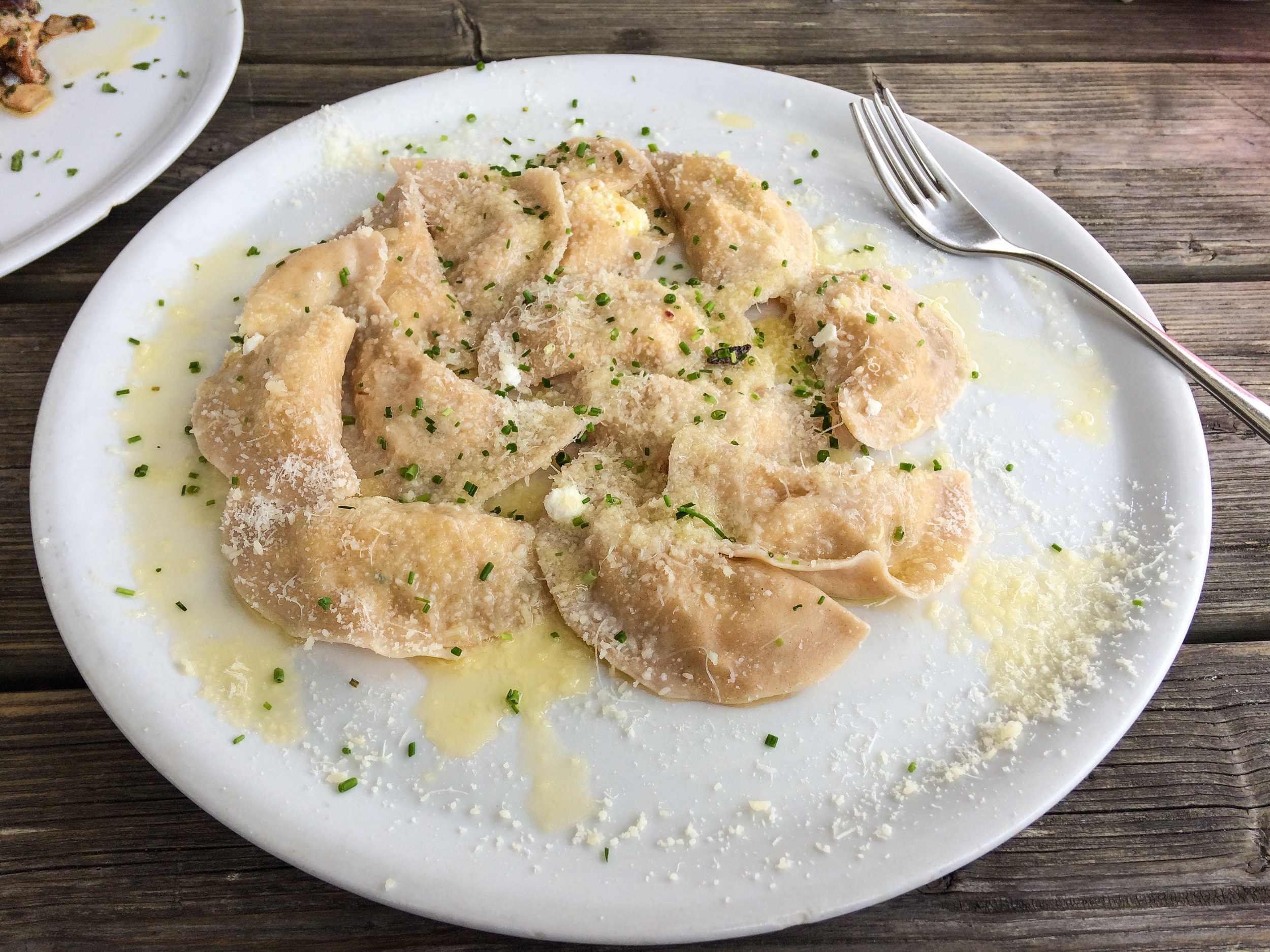 Filled dumplings served on a plate covered with parmesan, butter and chives