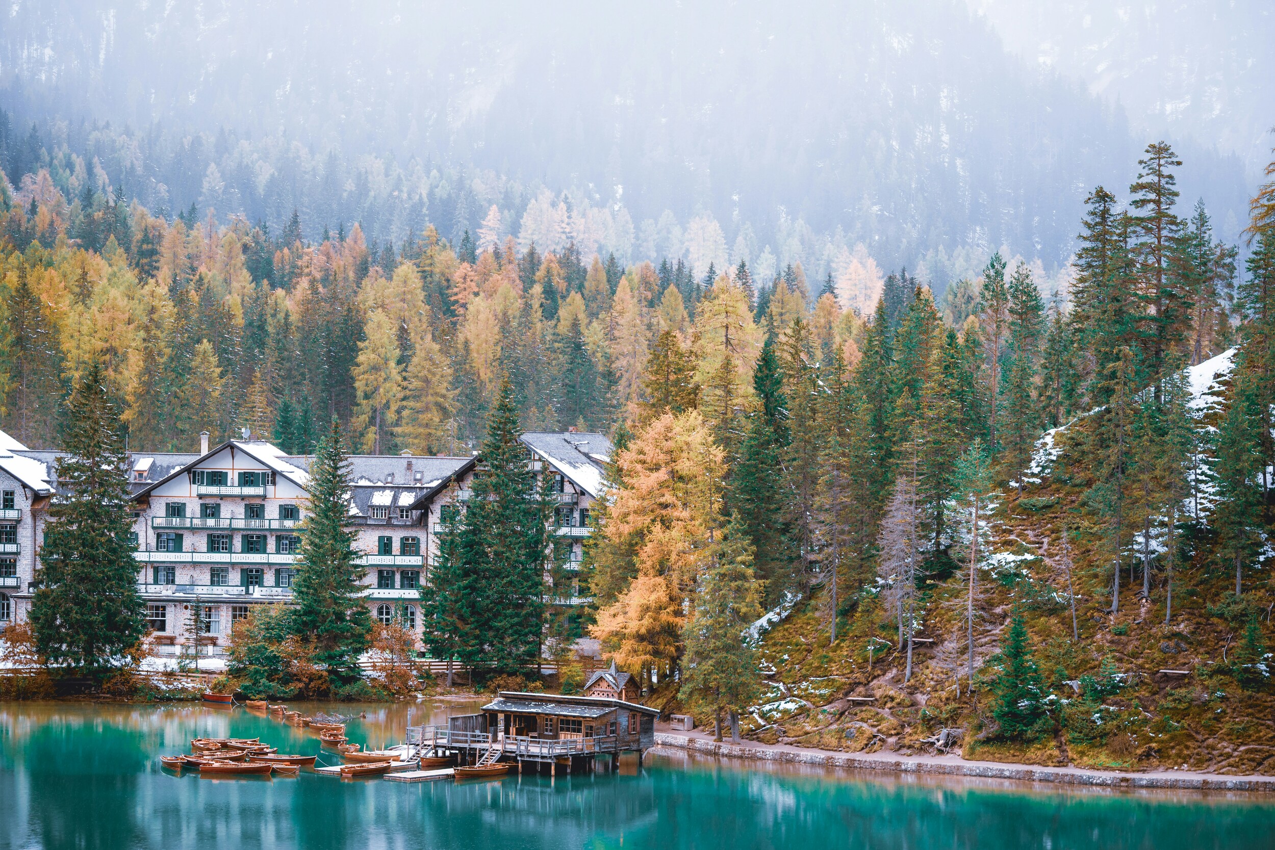 House surrounded by autumn-coloured trees, lakeshore with wooden boats in the foreground