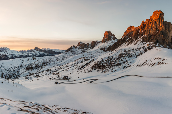 Snow landscape framing a mountain pass road with peaks lit by the last sunlight