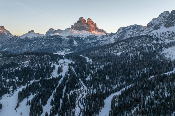 Pass road, snow-covered woods and peaks at sunrise