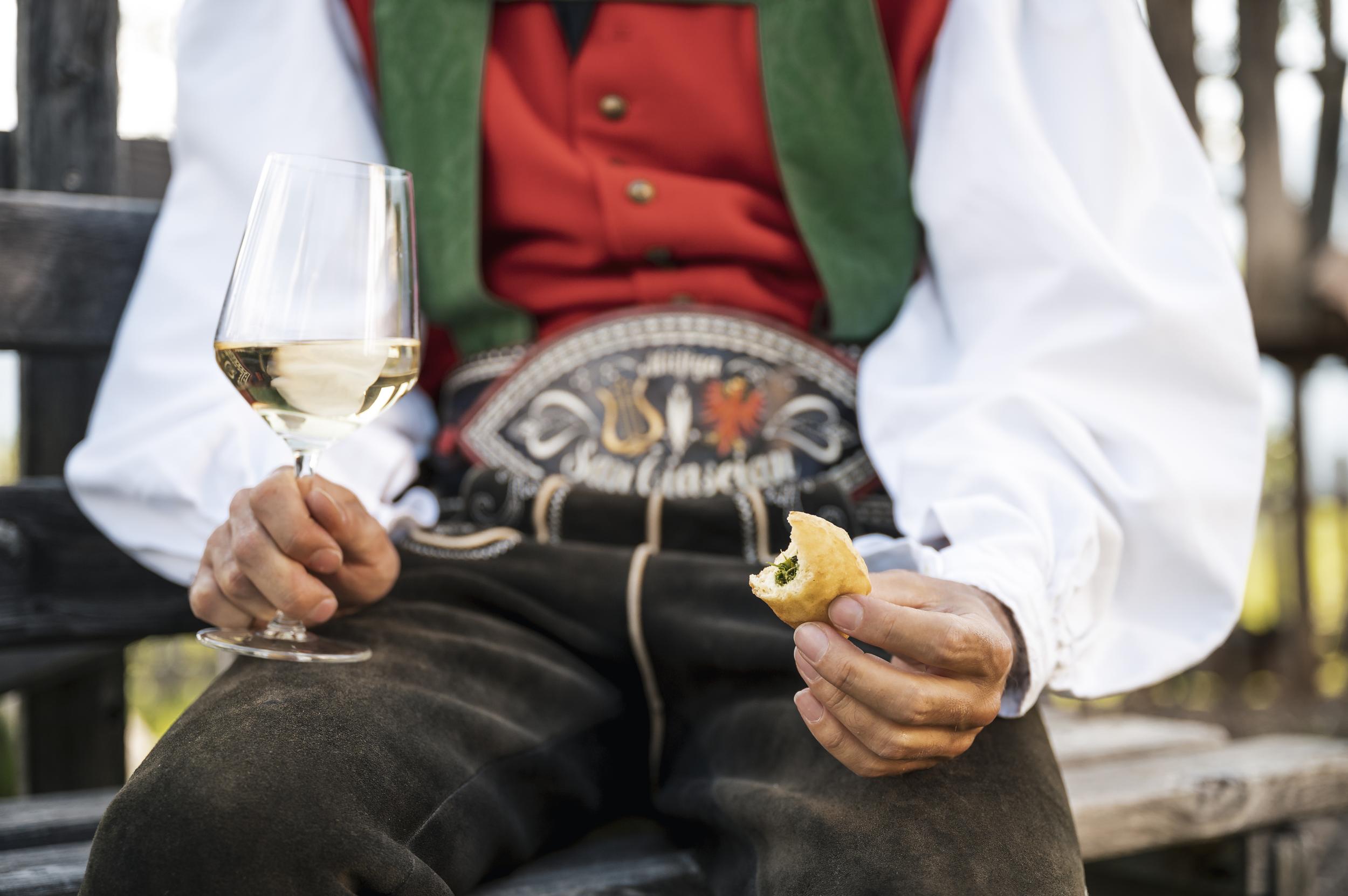 Man in a traditional costume with galss of white wine & pastry