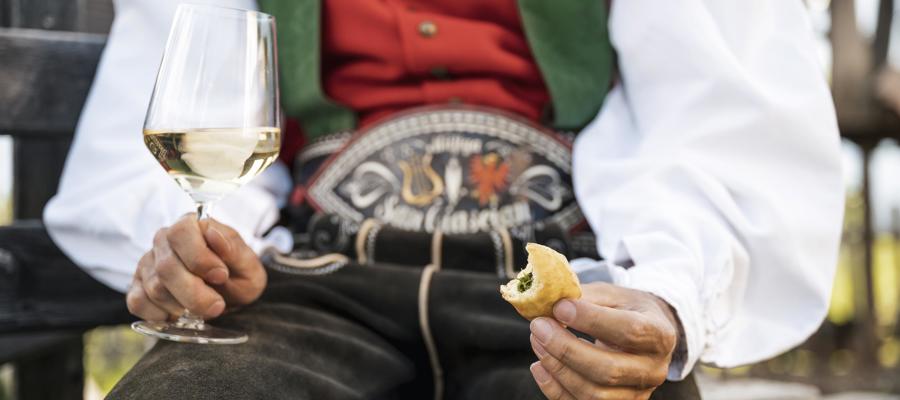 Man in a traditional costume with galss of white wine & pastry