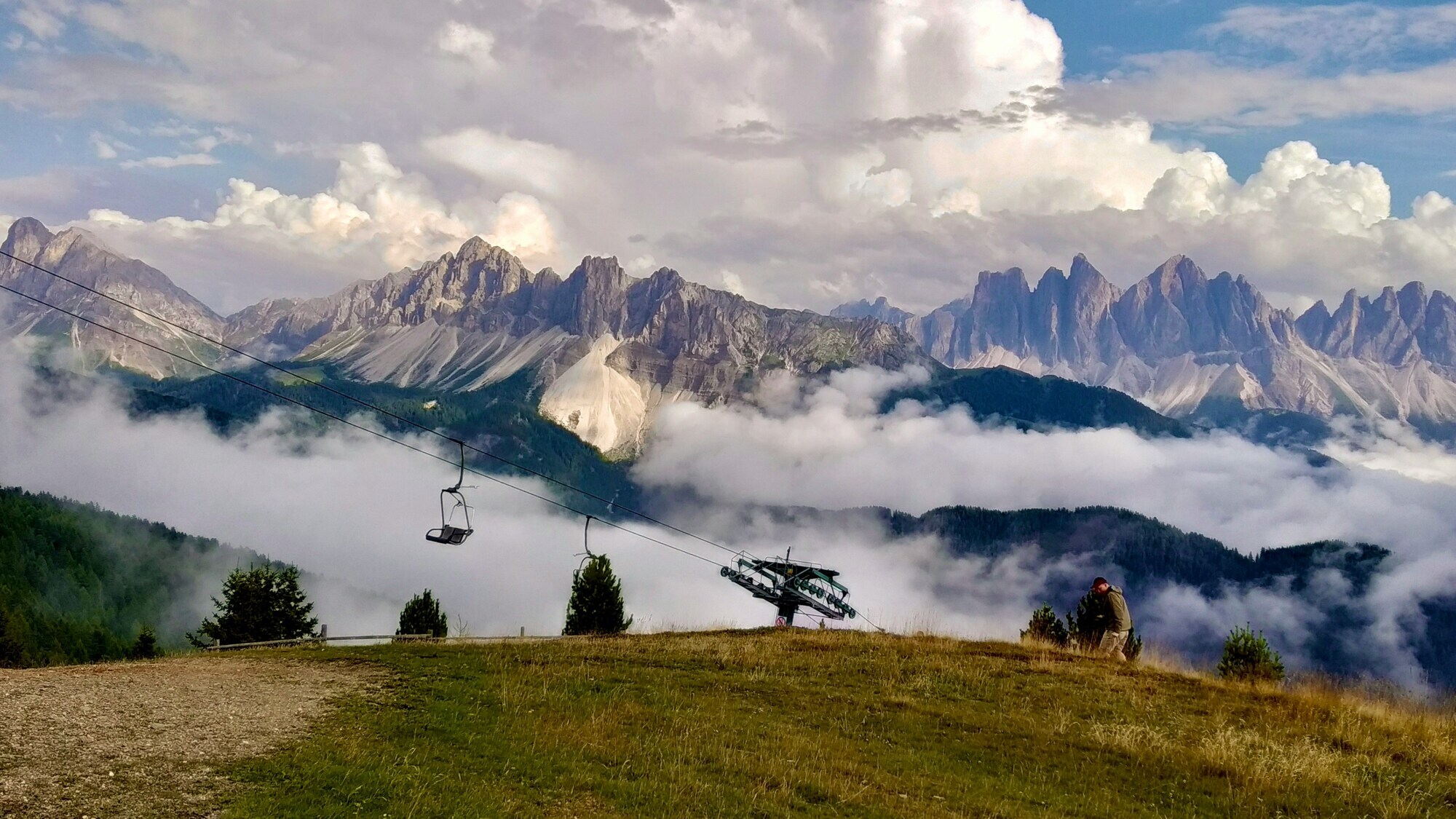 Hiker, chairlift and meadows in front of mountain range