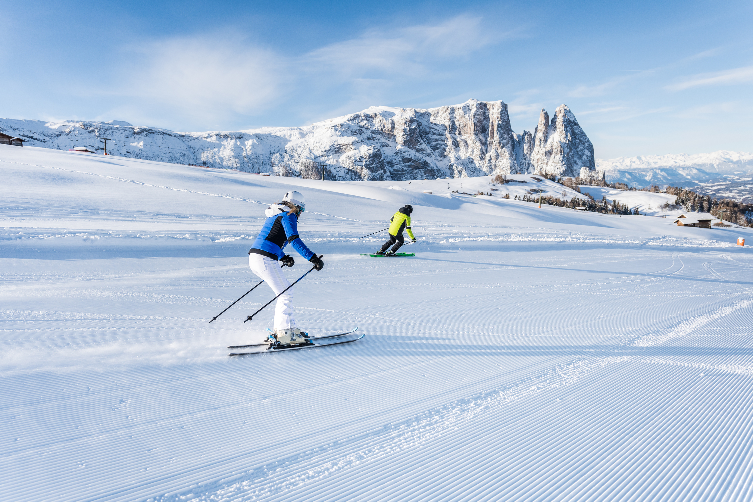 Two skiers on a prepared slope in front of a mountain range