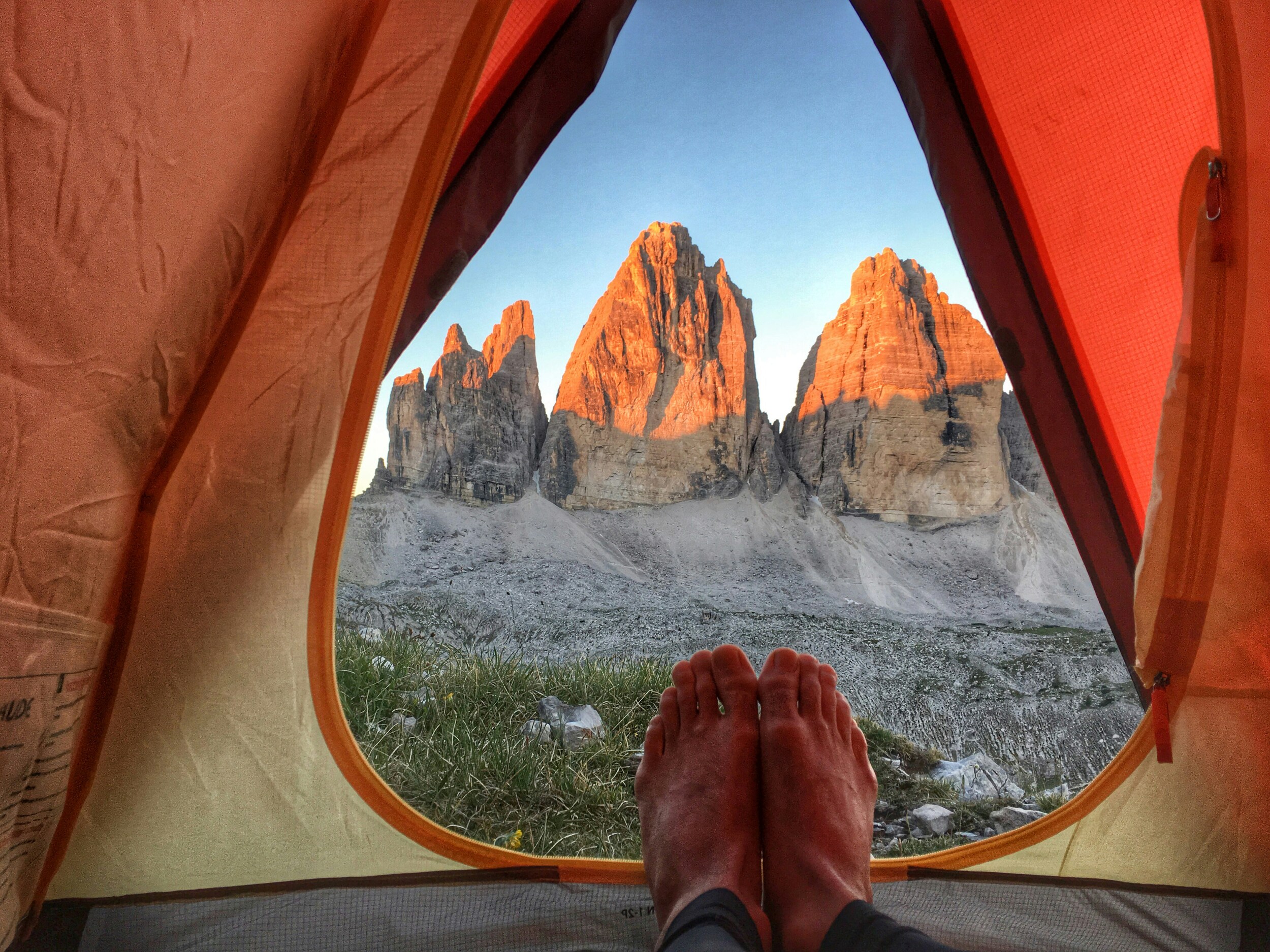 Feet of a man lying in an orange tent with mountain view