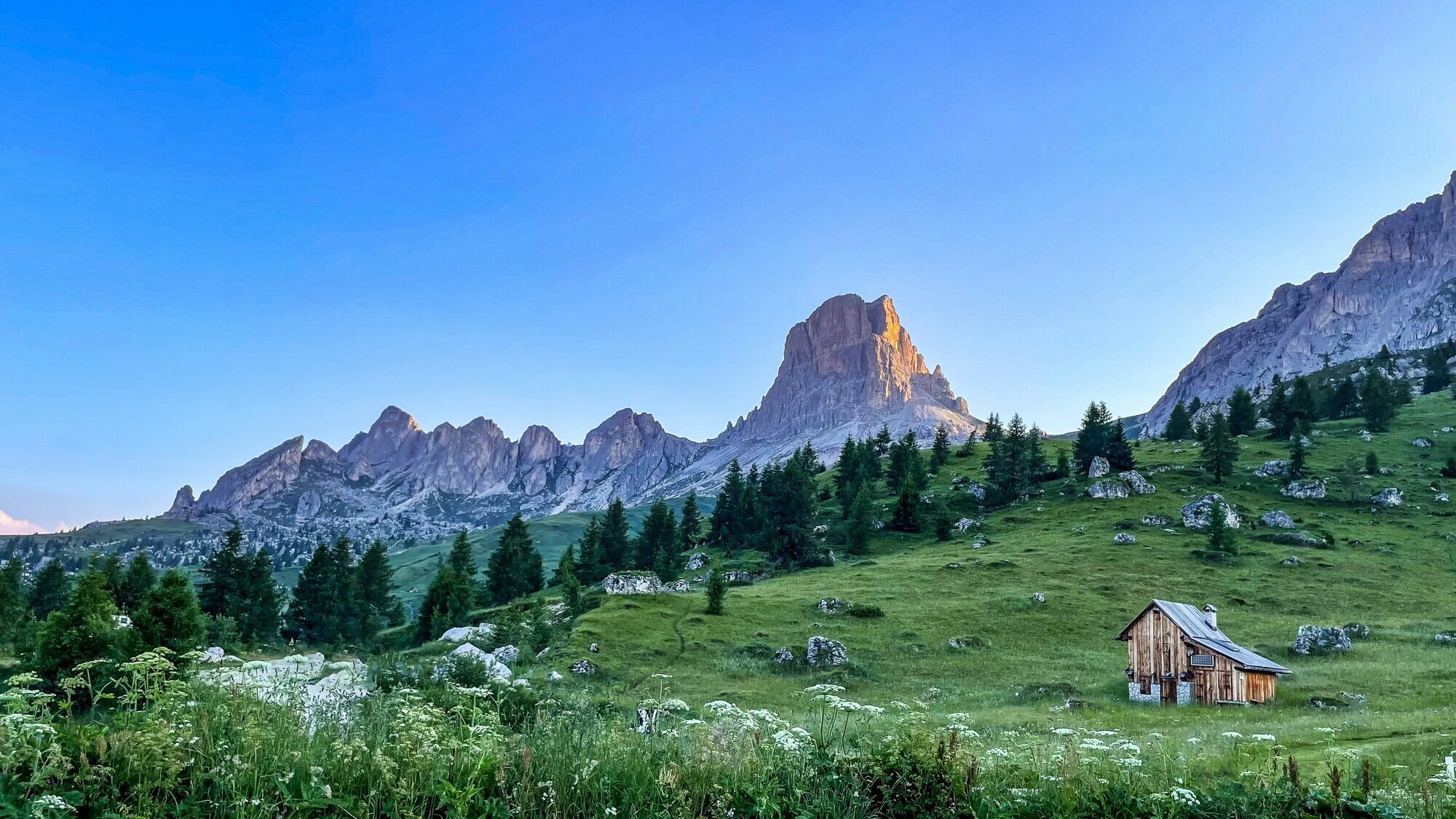 Mountains, alpine hut and meadows at sunset