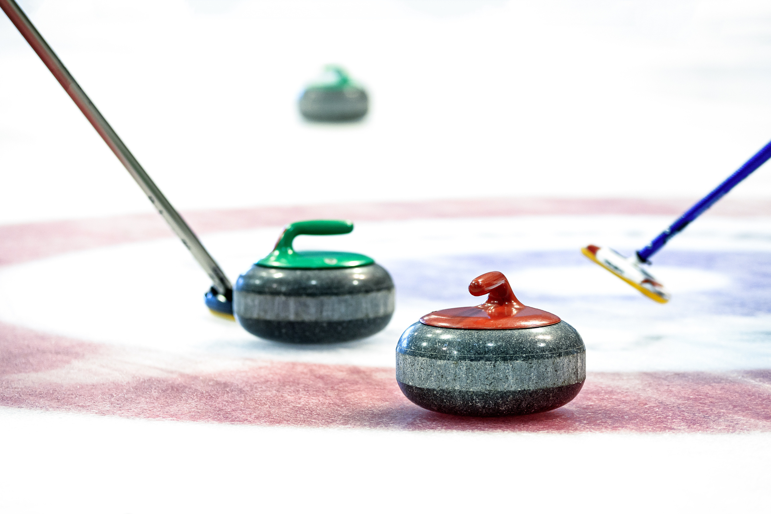 Two curling stones and brushes on the target circle on the ice