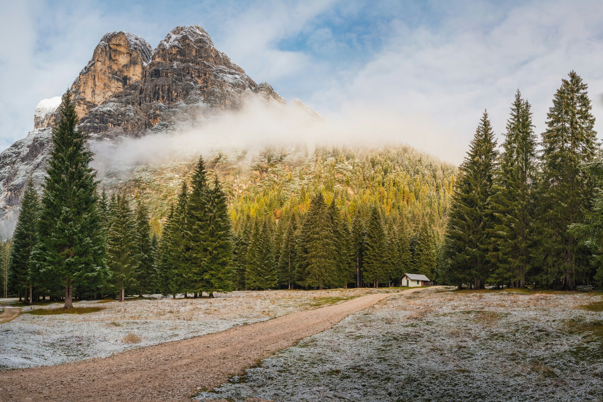 Lightly snow-covered meadow in the woods with road and small hut