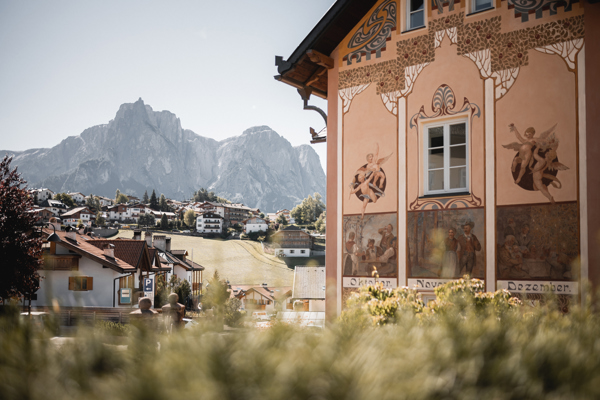 Historic house with artistic paintings, other houses and mountains behind it