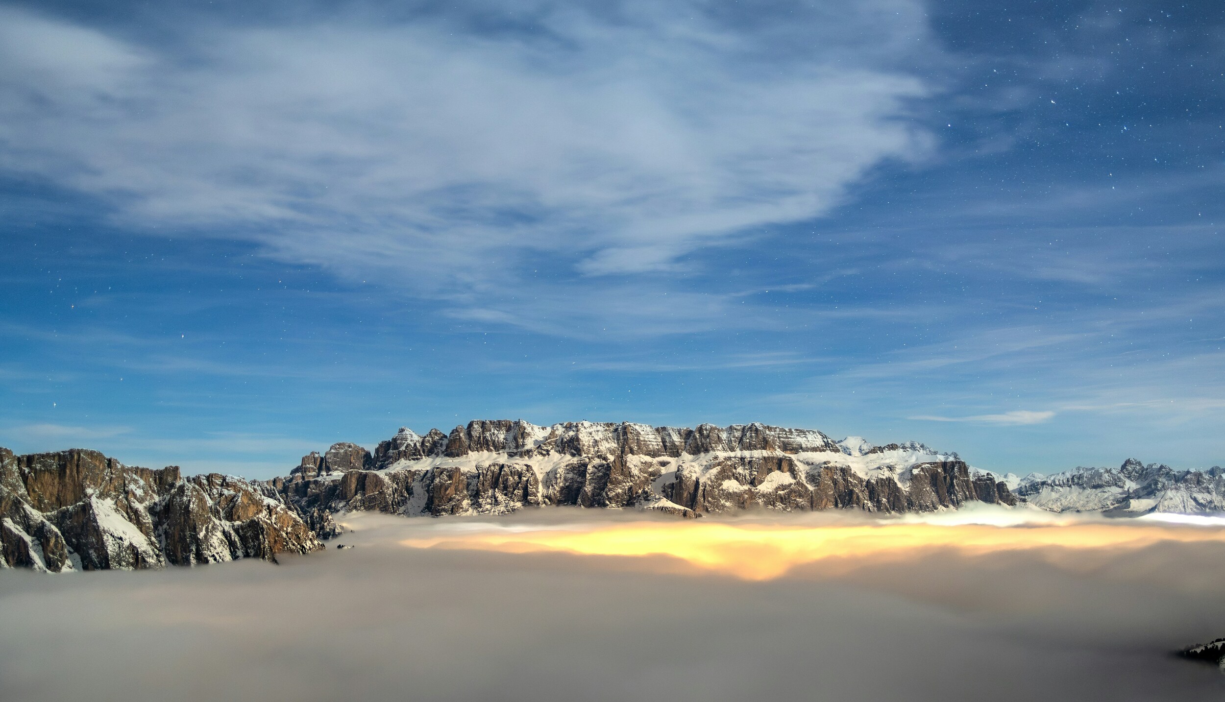 Valley covered with clouds and light below, snowy mountains