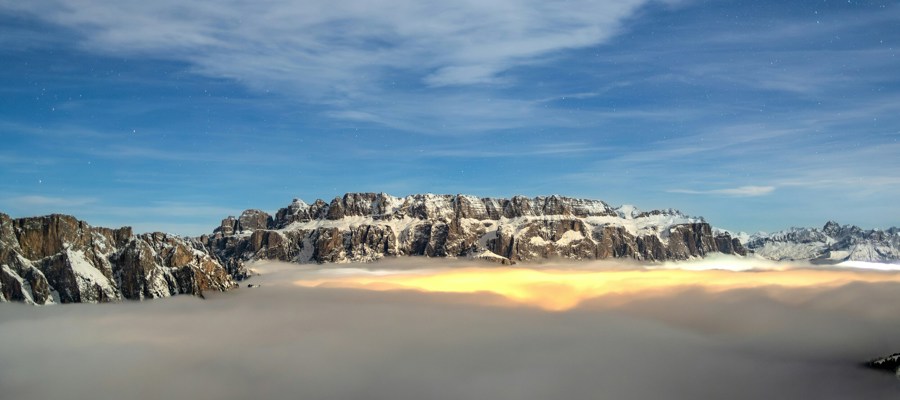 Valley covered with clouds and light below, snowy mountains