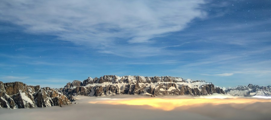 Valley covered with clouds and light below, snowy mountains