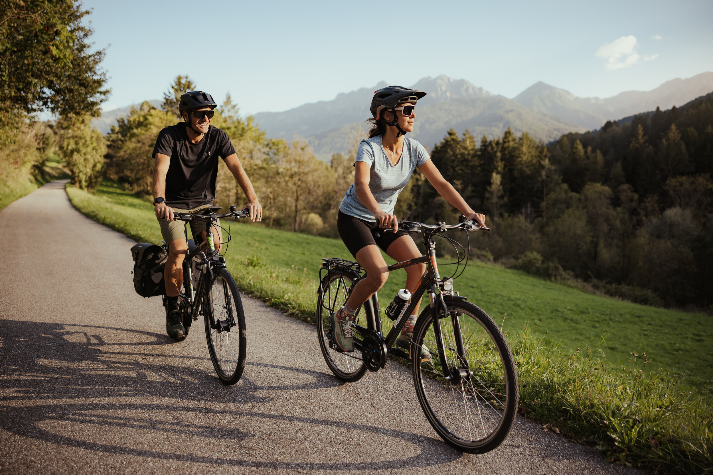 2 persons on bikes on a cycle path with forest and mountains